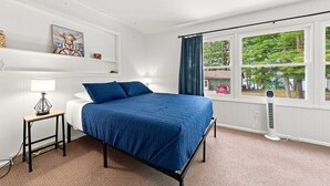 Un dormitorio con cama, mesita de noche, lámpara, ventana con cortinas y vistas al exterior.