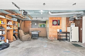 A basement with a foosball table, a dartboard, and a refrigerator.