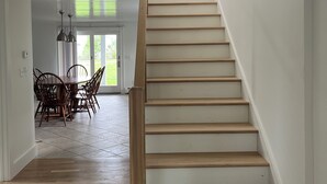 Un escalier avec des marches en bois et une rampe, menant à un palier doté d’un mur en pierre et offrant une vue sur un coin repas avec des chaises et une table.