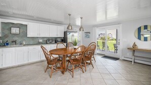 Une cuisine moderne avec des meubles blancs, une table à manger avec des chaises et des luminaires suspendus.