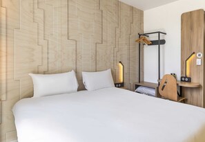 Ein Hotelzimmer mit einem großen Bett, einem Holz-Kopfteil, einem Nachttisch, einem Schreibtisch mit Stuhl und einem Kleiderschrank.