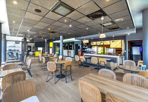 Ein modernes Café mit verschiedenen Sitzbereichen, darunter Tische und Stühle sowie eine Theke mit Speisekarte.