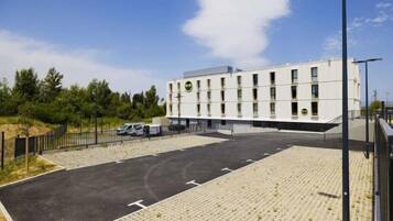 A building with a flat roof, a parking lot with marked spaces, and a fence surrounding the area.