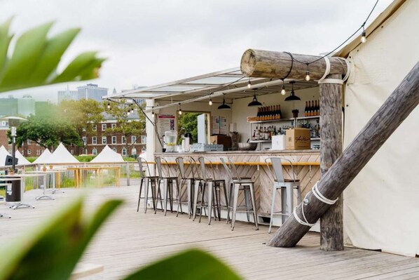An outdoor bar area with a wooden deck, bar stools, and a rustic wooden structure. - Canvas Retreats | Morning Yoga | City Escapes (New York)