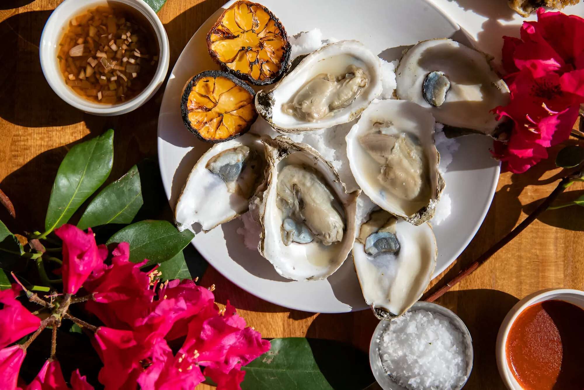 A plate of oysters with a side of pickled onions and a small bowl of sauce.