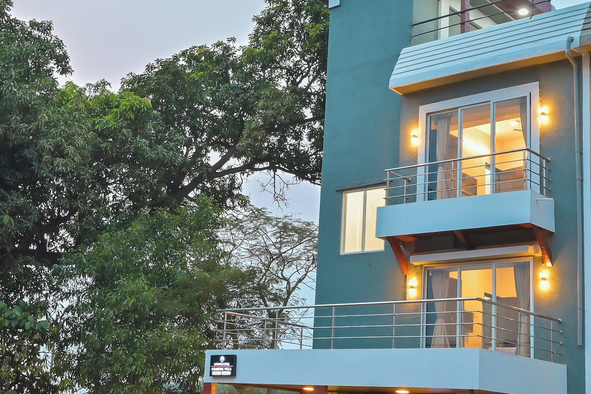 A multi-story hotel with a balcony on the upper floor, a gated entrance, and a view of trees.