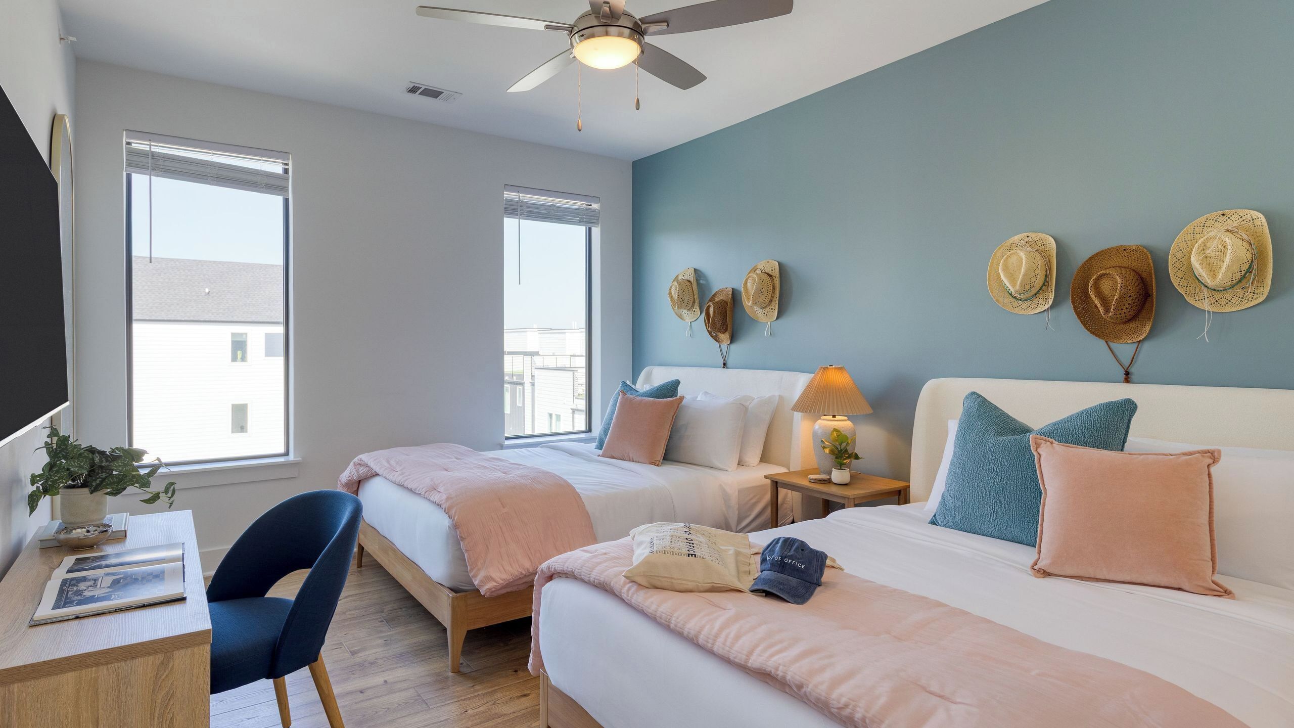 Une chambre d’hôtel avec deux lits, un bureau, une chaise, un ventilateur de plafond et une vue sur l’extérieur.