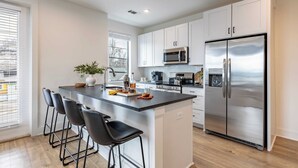 A modern kitchen with white cabinets, stainless steel appliances, and a central island with bar stools. - The Heights by AvantStay (Nashville)