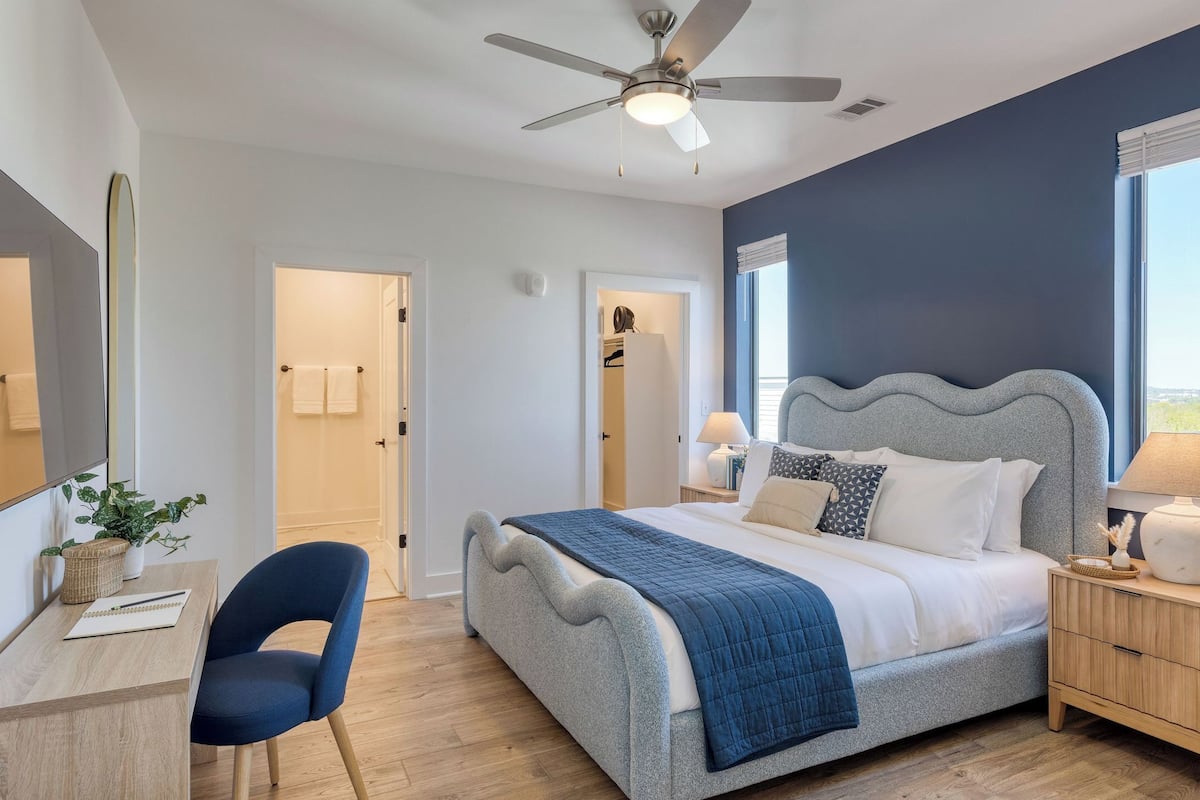 Un dormitorio con cama, mesita de noche, lámpara y un escritorio con silla.