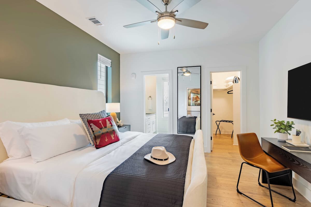 Habitación de hotel moderna con cama, escritorio, silla, ventilador de techo y televisor.