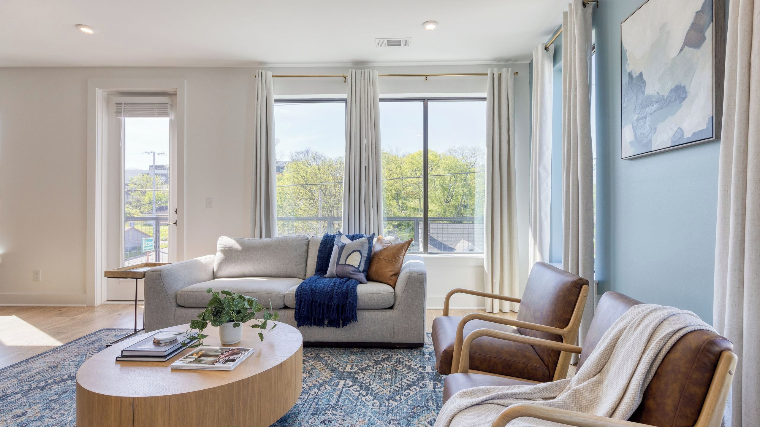 Una sala de estar moderna con sofá, sillón, mesa de centro y ventanas amplias.