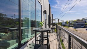 A balcony with a table and chairs, a potted plant, and a view of a street and buildings. - The Heights by AvantStay (Nashville)