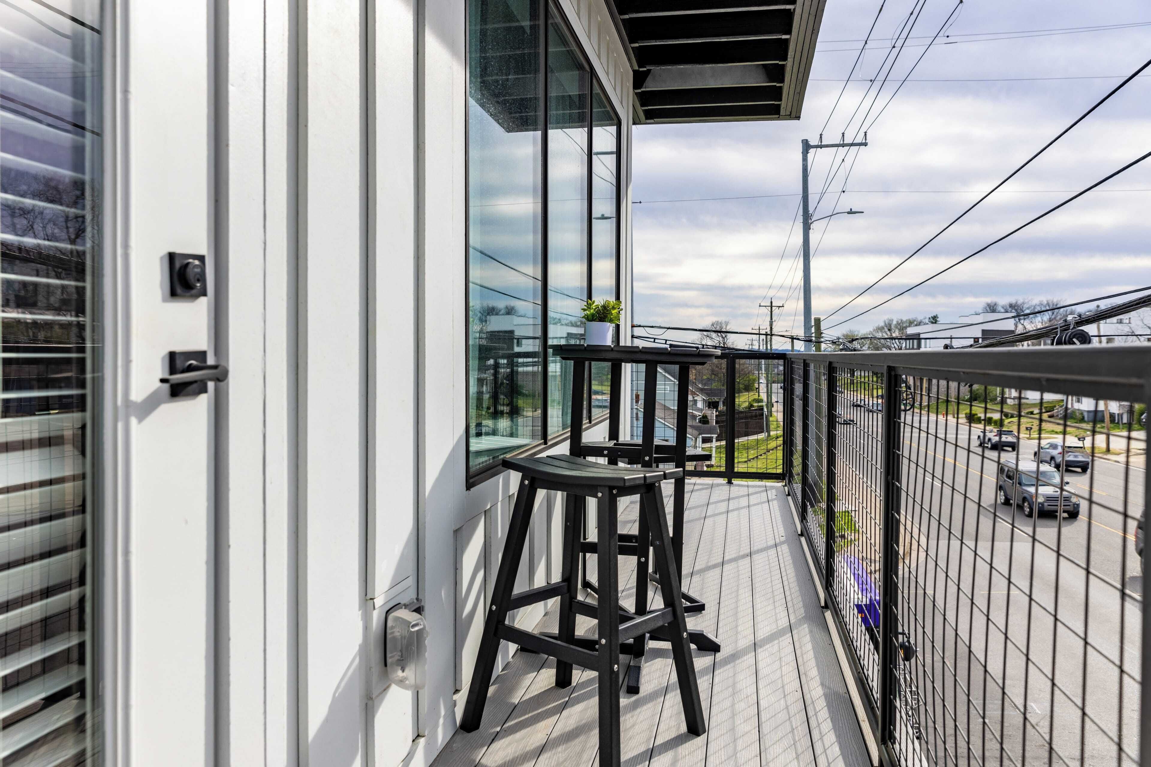 A balcony with a black metal railing, a small stool, and a potted plant.