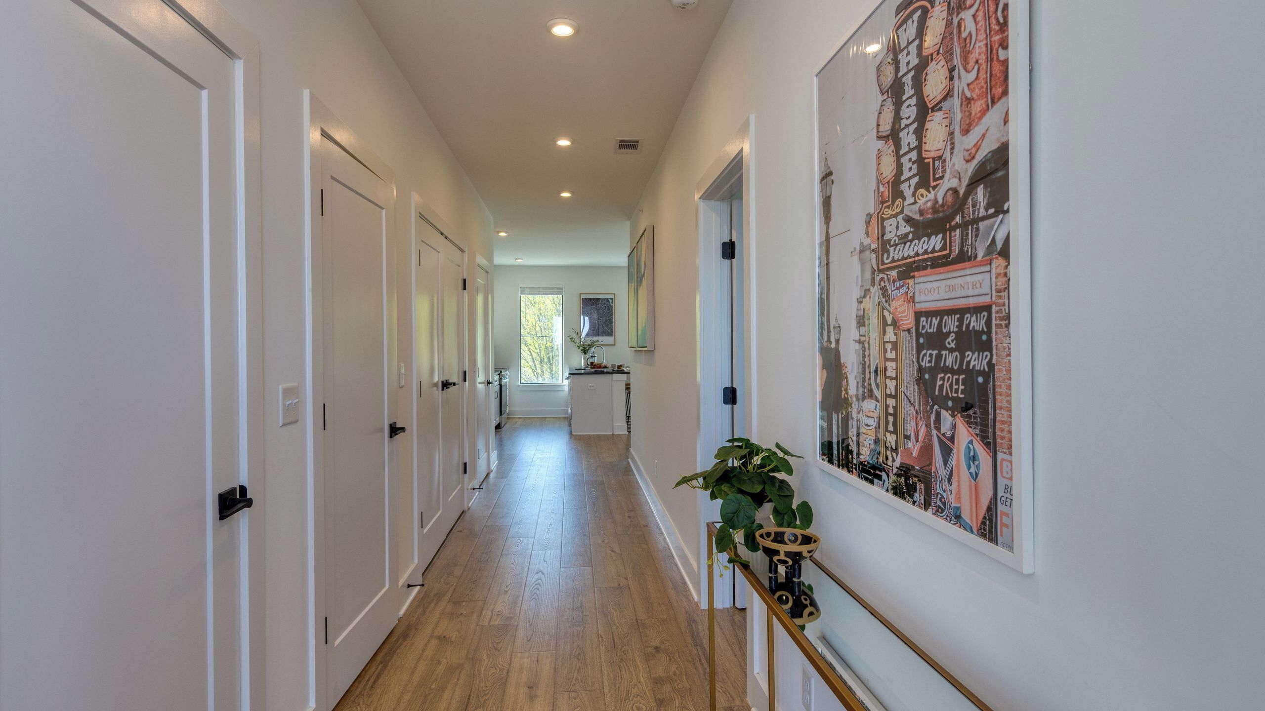 A hallway with white doors, a wooden floor, a plant, and a large poster on the wall.