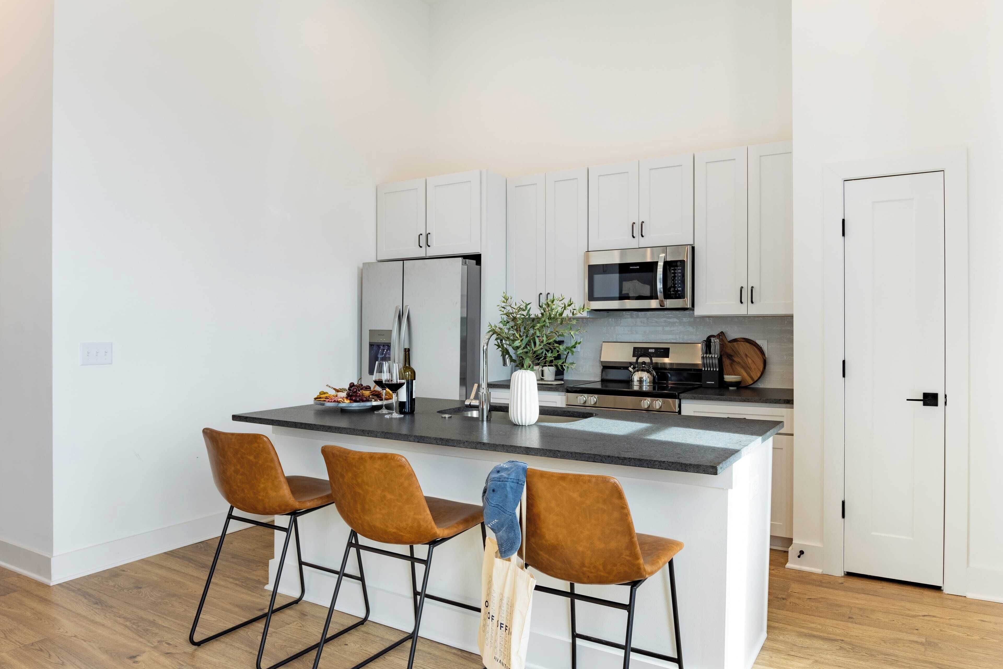A modern kitchen with white cabinets, a central island with bar stools, stainless steel appliances, and a potted plant.