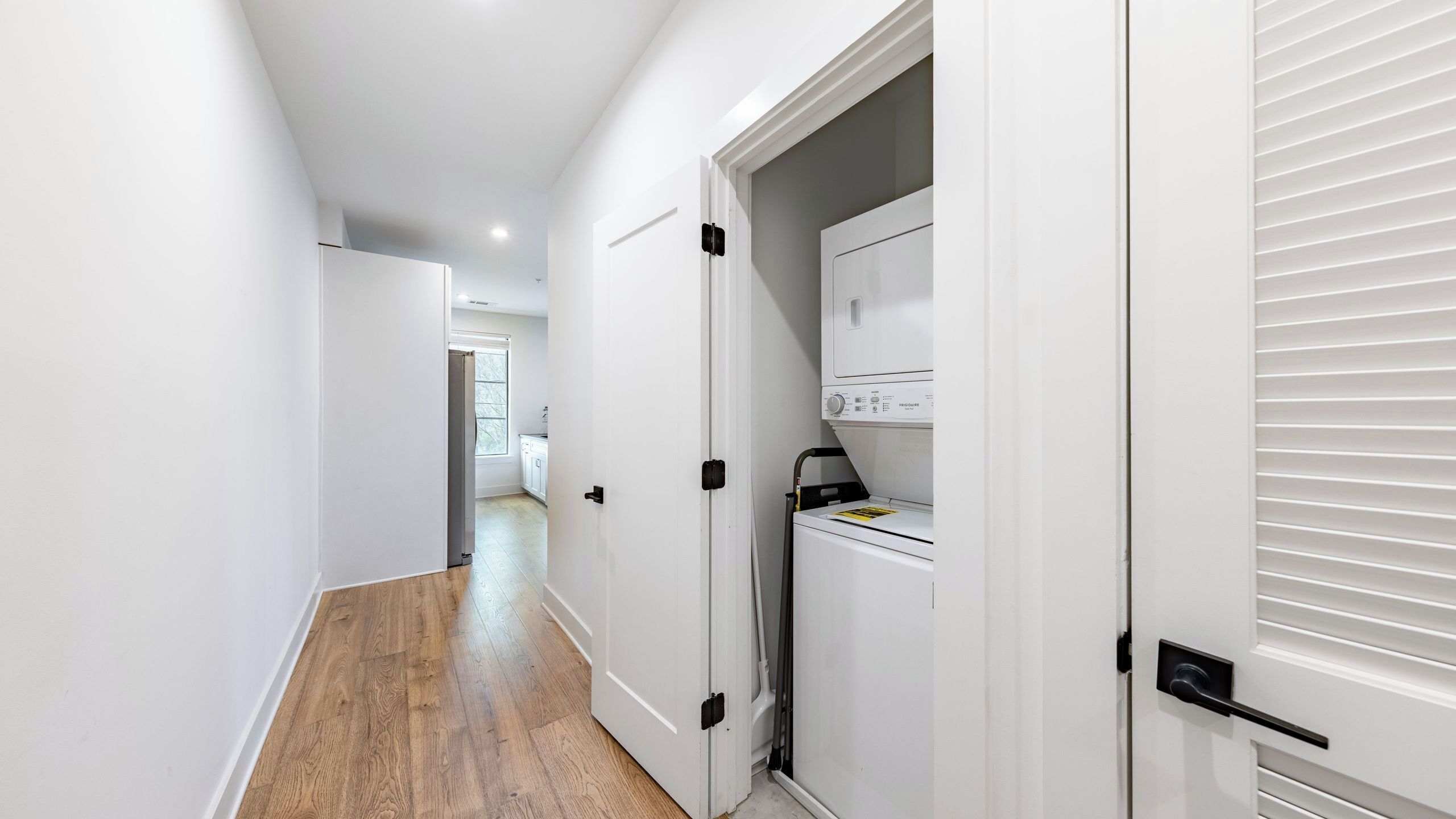 Un couloir doté d’un plancher en bois, de murs blancs et d’une porte donnant sur une buanderie équipée d’un lave-linge.