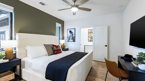 Une chambre à coucher moderne, avec un lit, des tables de chevet, un bureau, une chaise, un ventilateur de plafond et des œuvres d’art accrochées aux murs.
