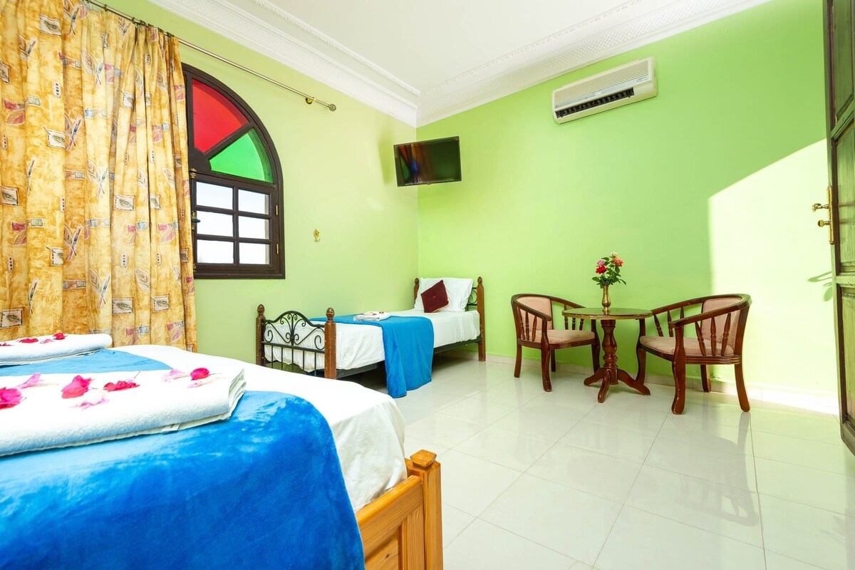 A hotel room with two beds, a small table with chairs, a TV, and a window with a curtain.