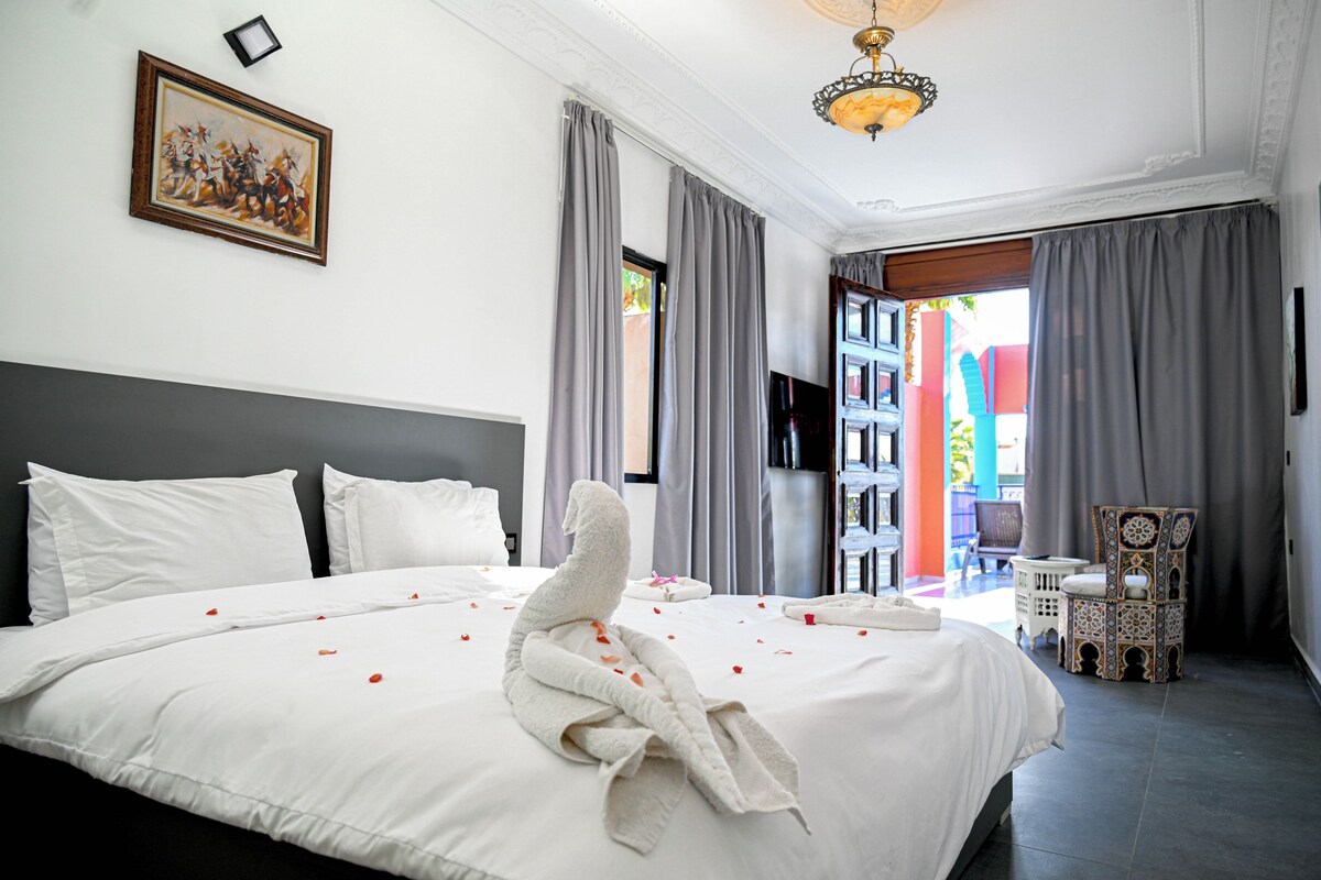A hotel room with a large bed, a flat-screen TV, a chandelier, and a view of the outside.