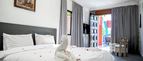 A hotel room with a large bed, a flat-screen TV, a chandelier, and a view of the outside.
