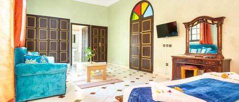 A hotel room with a large bed, a blue sofa, a wooden dresser, a TV, and a colorful stained glass window.