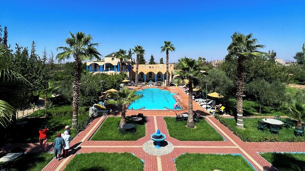 A pool area with a clear blue sky, palm trees, and a building in the background. - Riad Qodwa (Sidi Abdallah Ghiat)