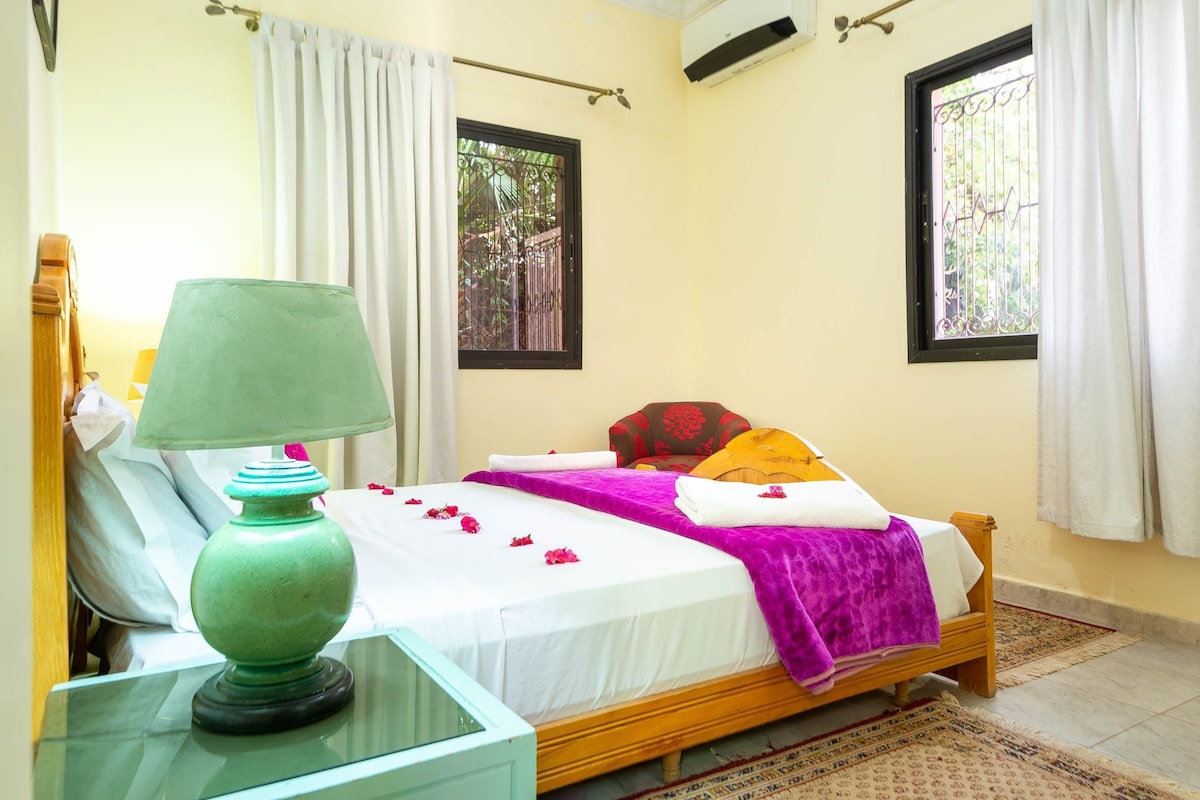 A room with a bed, a green lamp, and a window with a metal gate.