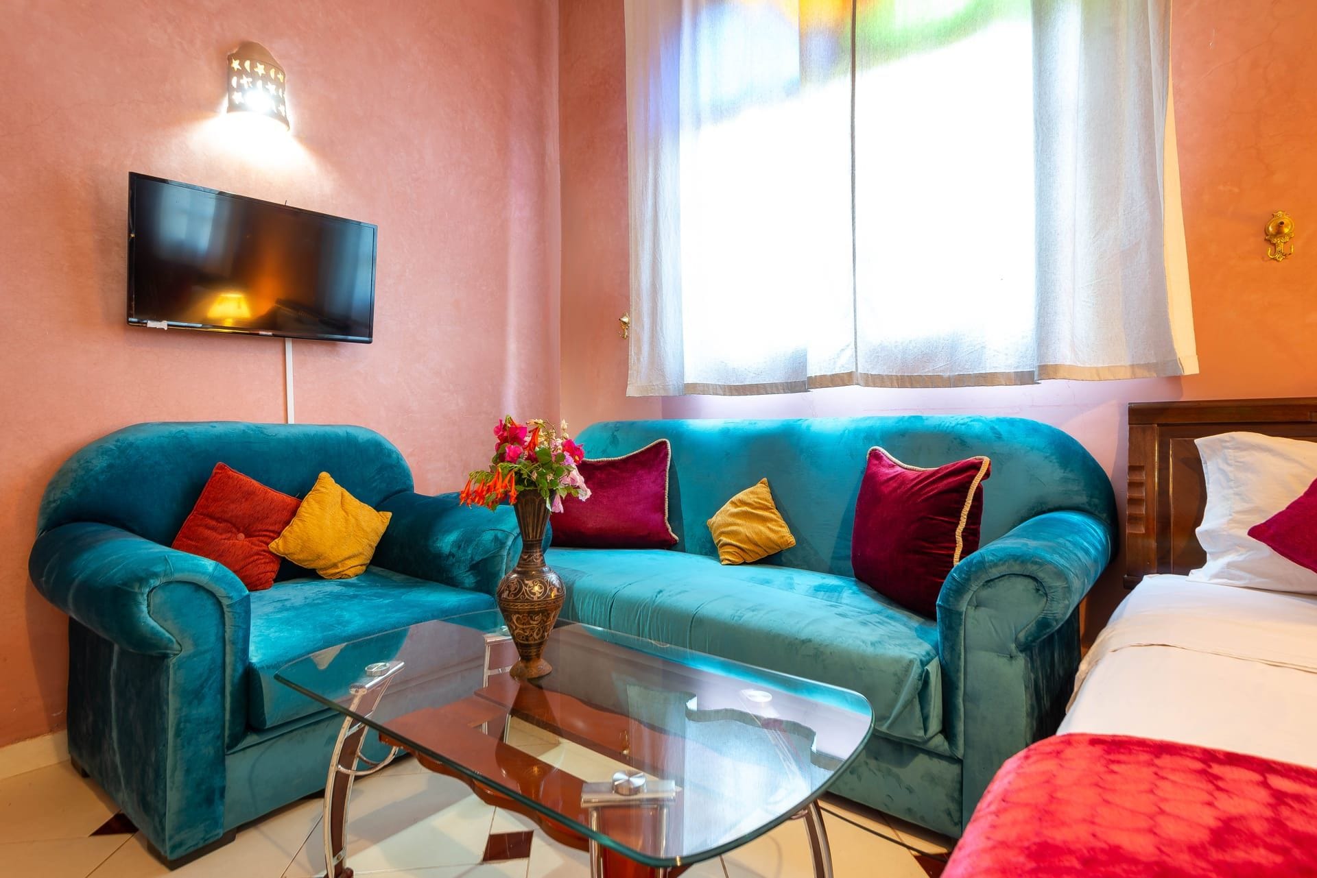 Una habitación con dos sofás color turquesa, una mesa de centro de vidrio, un televisor de pantalla plana en la pared y una ventana con cortinas translúcidas.