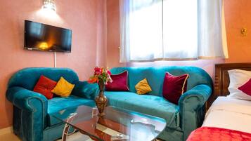 Una habitación con dos sofás color turquesa, una mesa de centro de vidrio, un televisor de pantalla plana en la pared y una ventana con cortinas translúcidas.