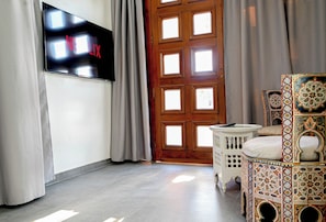 Une pièce dotée d’un téléviseur à écran plat fixé au mur, d’une porte en bois ornée de plusieurs fenêtres et d’un pouf à motifs.
