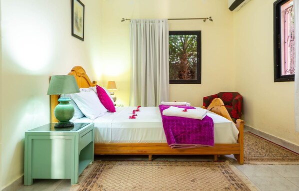 A bedroom with a bed, nightstands, a chair, a window with a view of trees, and a curtain. - Riad Qodwa (Sidi Abdallah Ghiat)