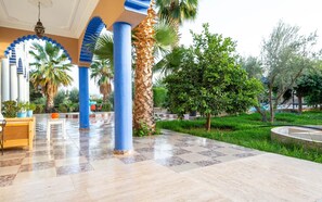 A covered outdoor area with tiled flooring, blue pillars, and palm trees. - Riad Qodwa (Sidi Abdallah Ghiat)