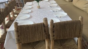 A dining area with a long table set for a meal, surrounded by wicker chairs. There are hanging lights above the table, and the walls are adorned with framed artwork. - Riad Qodwa (Sidi Abdallah Ghiat)