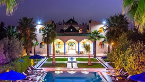 A hotel with a pool, palm trees, and a well-lit courtyard. - Riad Qodwa (Sidi Abdallah Ghiat)