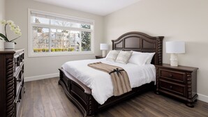 A bedroom with a large bed, two bedside tables, a dresser, and a window with a view of buildings.