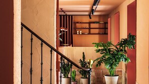 Una escalera con barandilla negra que lleva a una habitación con un muro rojo de acento, un estante de madera y plantas en macetas.