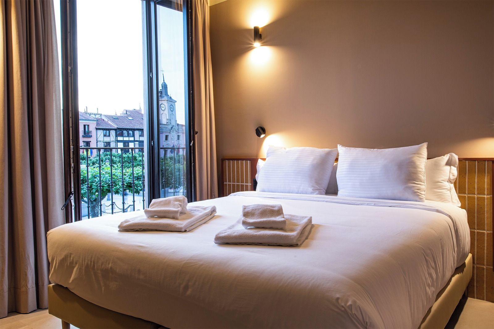 Habitación de hotel con una cama grande, dos almohadas, una mesita de noche y una ventana con cortinas.