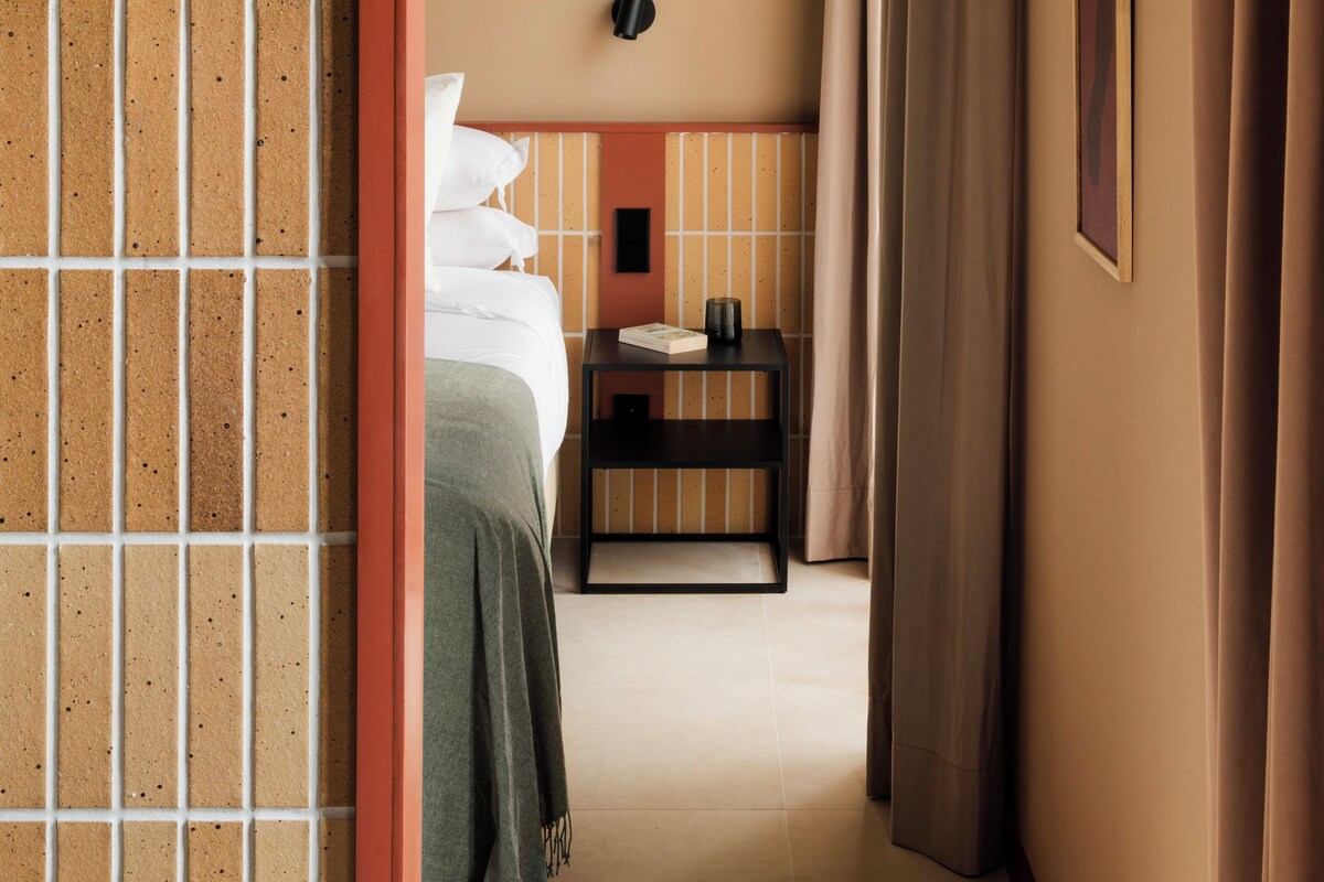 A hotel room with a bed, bedside table, and a view of the hallway.