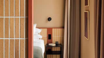 Una habitación de hotel con cama, mesita de noche y vista al pasillo.