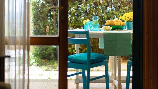 Una mesa de comedor con sillas, un frutero y un florero con flores amarillas.