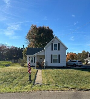 A two-story white house with a front porch, a small shed, and a lawn.