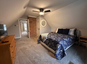 A bedroom with a bed, a ceiling fan, a brick wall, and a door leading to another room. - Relax and Roscoe Apartment (Coshocton)