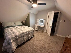 A bedroom with a bed, a desk with a mirror, a ceiling fan, and a door. - Relax and Roscoe Apartment (Coshocton)