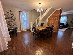 A dining area with a wooden table and chairs, a chandelier, and a staircase leading to an upper level. - Relax and Roscoe Apartment (Coshocton)