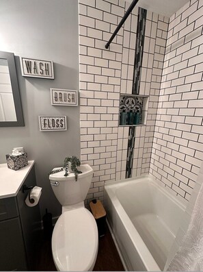 A bathroom with a toilet, sink, and bathtub. There are signs on the wall that read "WASH," "BRUSH," and "FLOSS."