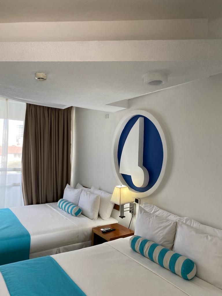 A hotel room with two beds, a large wall clock, a nightstand, and a window with curtains.