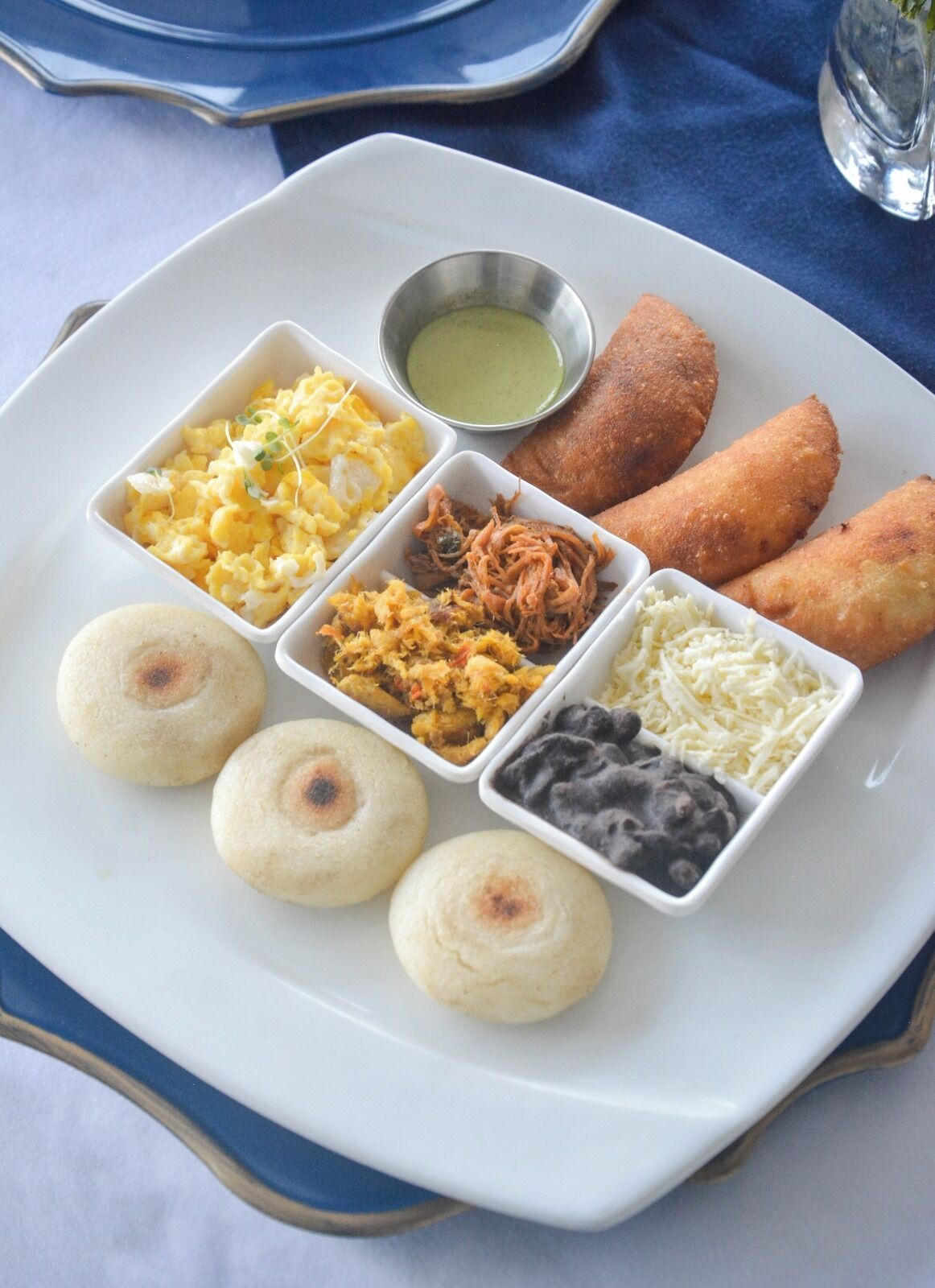 A plate with various food items including scrambled eggs, pulled pork, cheese, and black beans.