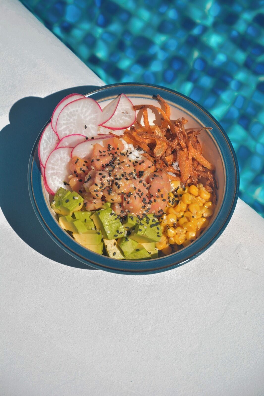 Un tazón de comida con diversos ingredientes, como aguacate, maíz y rodajas de rábanos.