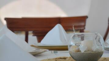 A dining table set with plates, cutlery, and a centerpiece of a glass bowl with sand and shells.