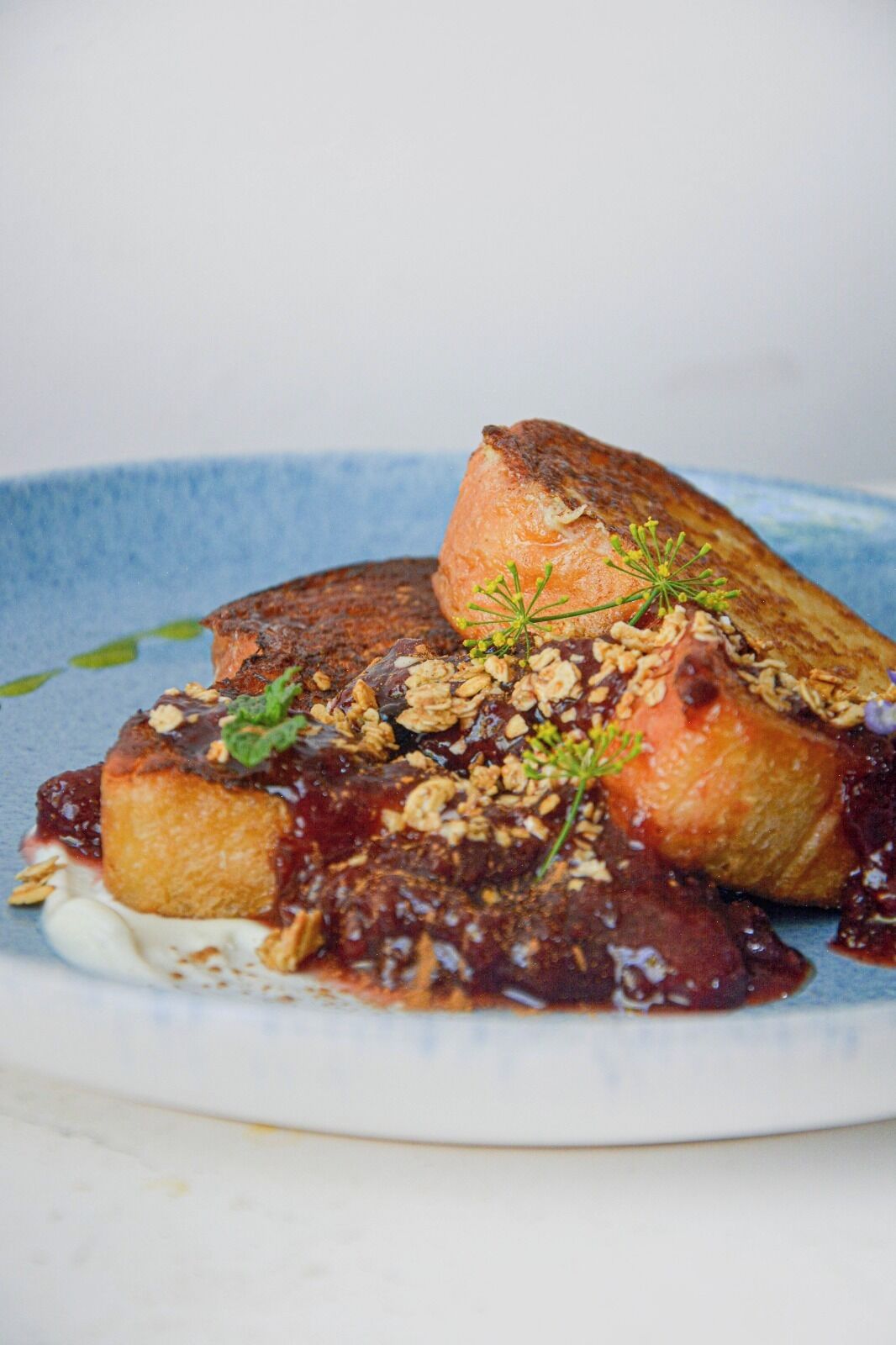 Een nagerechtenbord met een stuk taart, bestrooid met granola en een bessenjus.